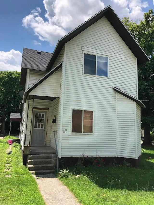 rear view of house featuring a lawn and roof with shingles