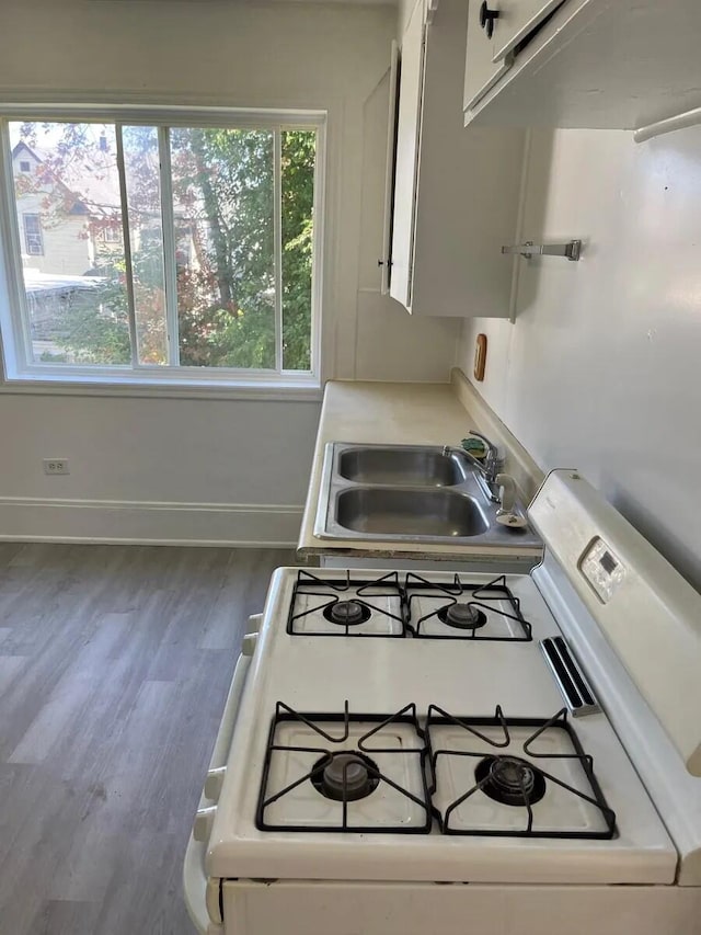 kitchen with baseboards, gas range gas stove, light countertops, wood finished floors, and a sink