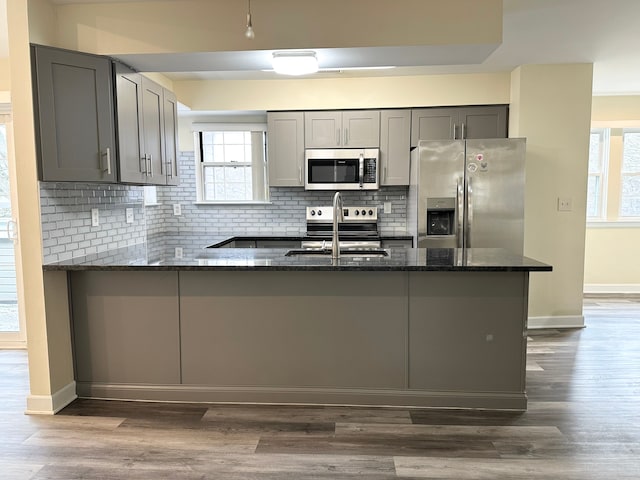 kitchen featuring dark stone counters, a peninsula, appliances with stainless steel finishes, and gray cabinetry