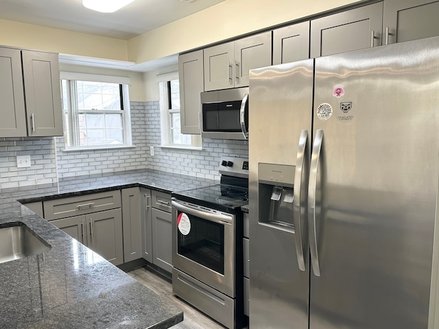 kitchen featuring backsplash, gray cabinets, appliances with stainless steel finishes, and dark stone countertops