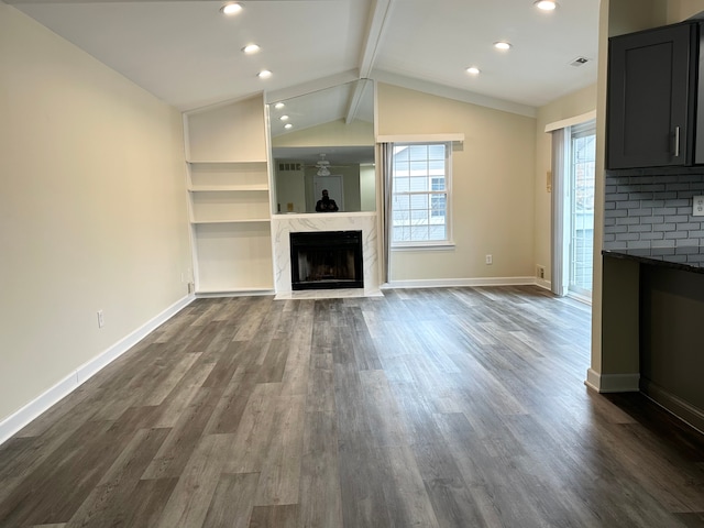 unfurnished living room featuring a healthy amount of sunlight, a fireplace, lofted ceiling with beams, and dark wood-style flooring