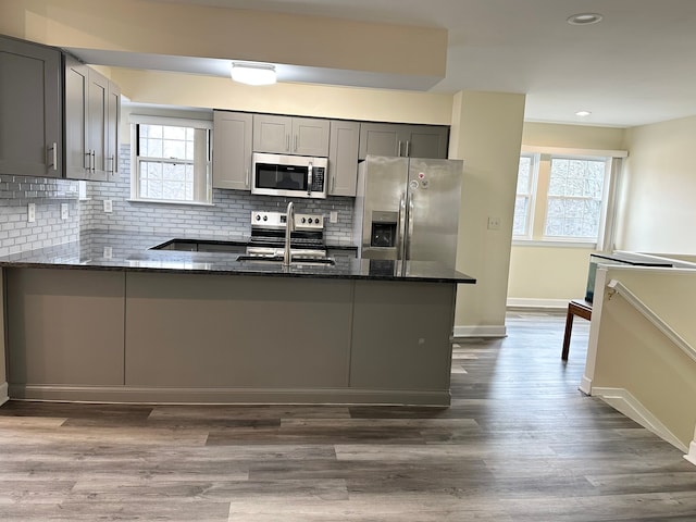 kitchen with dark stone counters, a peninsula, a sink, gray cabinetry, and stainless steel appliances