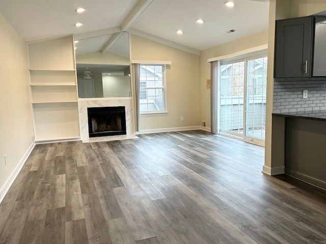 unfurnished living room featuring lofted ceiling with beams, dark wood finished floors, a wealth of natural light, and a high end fireplace