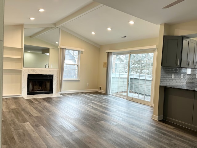 unfurnished living room featuring lofted ceiling with beams, baseboards, dark wood-type flooring, and a high end fireplace