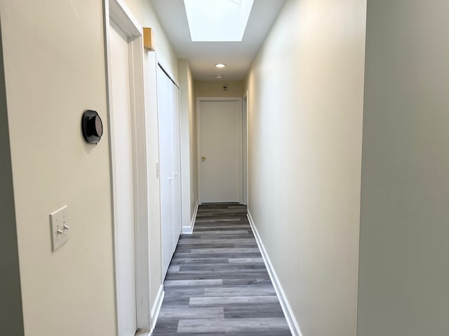 hall with wood finished floors, baseboards, and a skylight