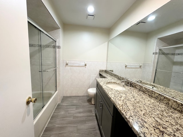 bathroom featuring vanity, visible vents, tile walls, toilet, and combined bath / shower with glass door