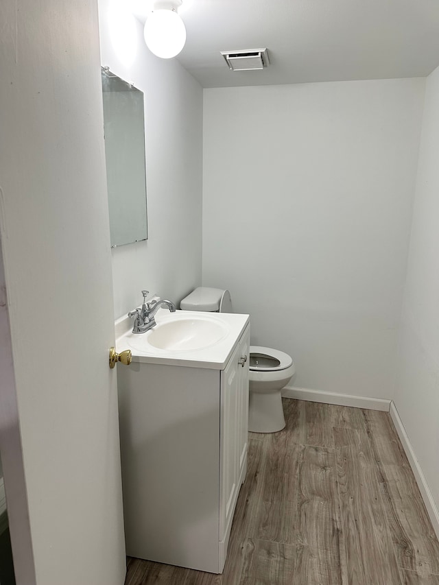 half bathroom featuring vanity, wood finished floors, visible vents, baseboards, and toilet