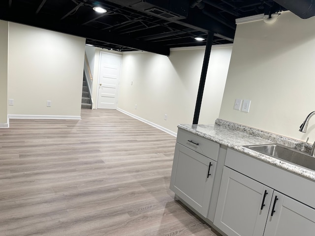 finished below grade area with visible vents, a sink, light wood finished floors, baseboards, and stairs