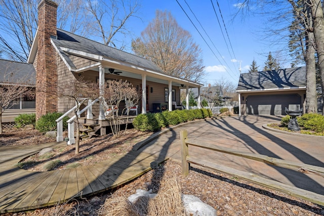 exterior space with covered porch, a shingled roof, a garage, ceiling fan, and a chimney