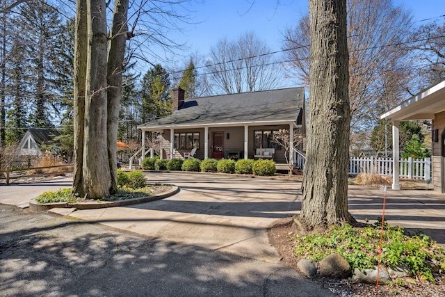 view of front of home with covered porch, a chimney, and fence