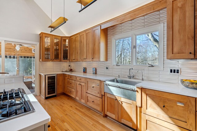 kitchen with light wood-type flooring, beverage cooler, stainless steel gas stovetop, light countertops, and lofted ceiling