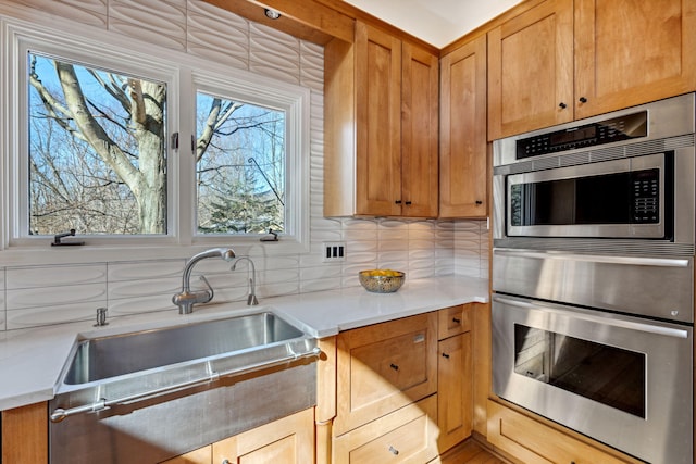 kitchen featuring backsplash, double oven, light countertops, brown cabinetry, and a sink