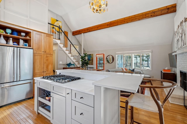 kitchen with lofted ceiling with beams, open shelves, a fireplace, light wood-style floors, and appliances with stainless steel finishes