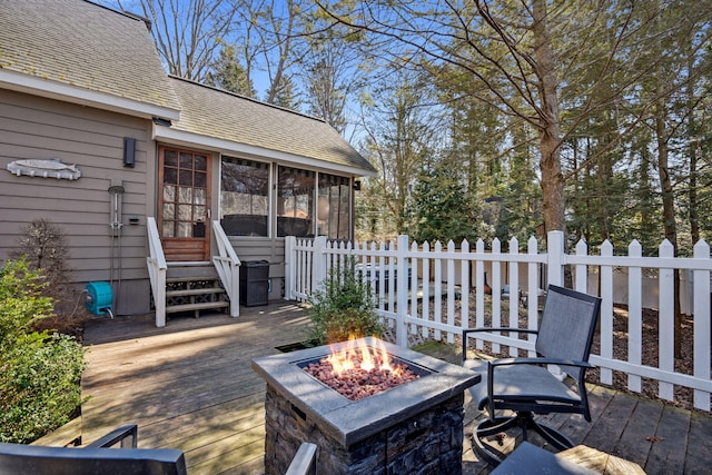 wooden deck featuring a fire pit, fence, and a sunroom