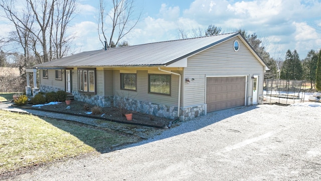 view of front of property with gravel driveway, a trampoline, metal roof, a garage, and stone siding