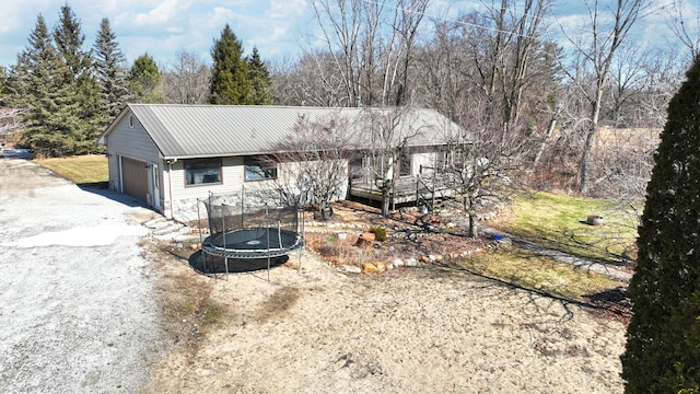 single story home featuring an attached garage, a trampoline, driveway, and metal roof