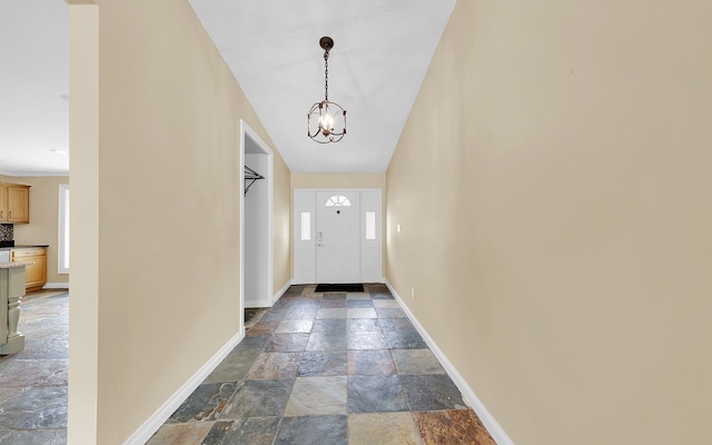 foyer featuring stone tile flooring, a chandelier, and baseboards