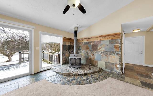 living room with ceiling fan, lofted ceiling, a wood stove, and stone tile flooring