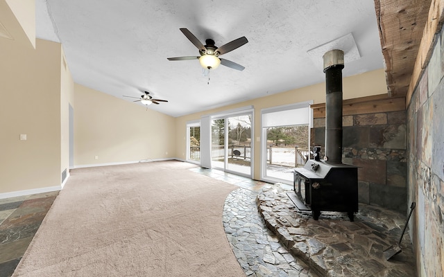 carpeted living area featuring baseboards, vaulted ceiling, a wood stove, a textured ceiling, and a ceiling fan