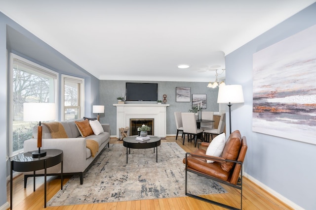 living room with a glass covered fireplace, baseboards, a notable chandelier, and wood finished floors