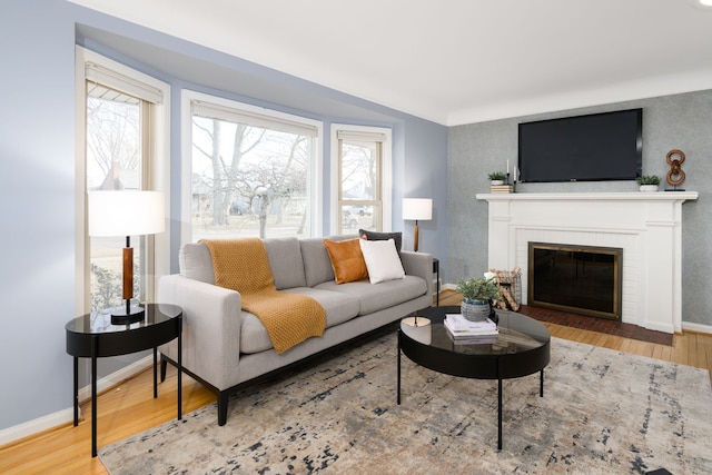 living area with baseboards, a brick fireplace, and wood finished floors