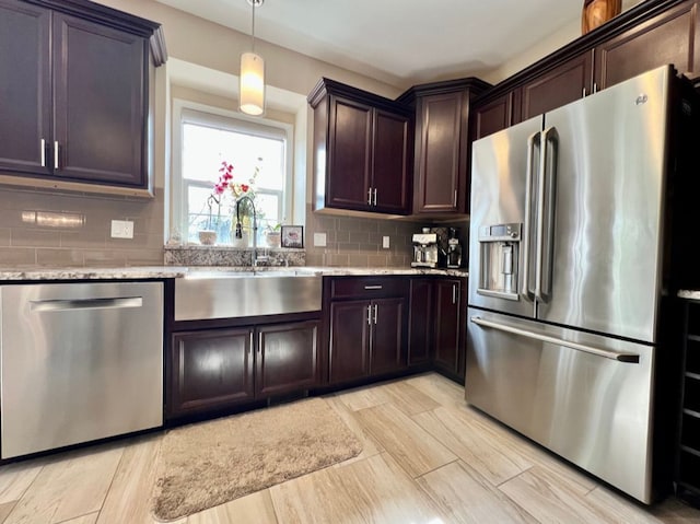 kitchen with light stone countertops, a sink, dark brown cabinetry, appliances with stainless steel finishes, and tasteful backsplash