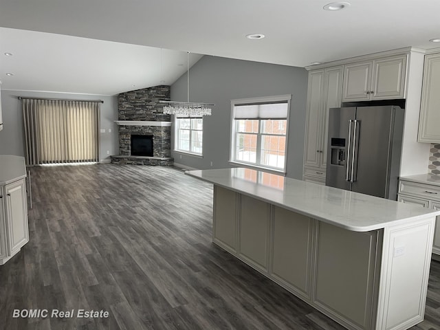 kitchen with dark wood-style floors, lofted ceiling, a stone fireplace, high end refrigerator, and a center island