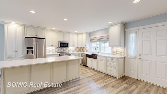 kitchen with stainless steel appliances, light countertops, a sink, a kitchen island, and decorative backsplash
