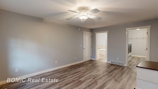 unfurnished bedroom with wood finished floors, a closet, a spacious closet, baseboards, and visible vents