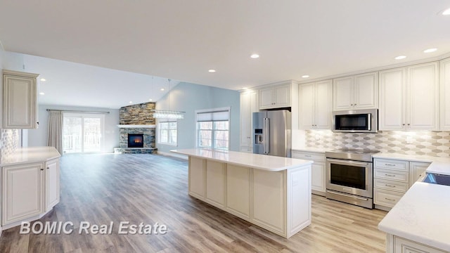 kitchen with stainless steel appliances, light countertops, a center island, a fireplace, and tasteful backsplash