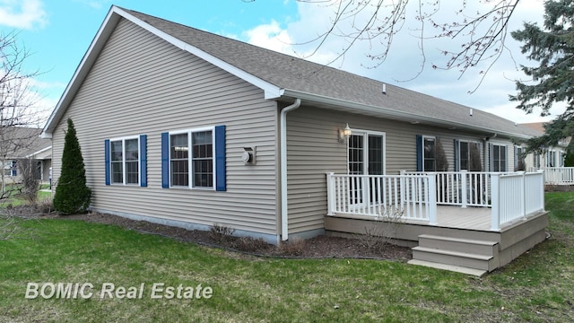 rear view of property with a wooden deck, roof with shingles, and a yard