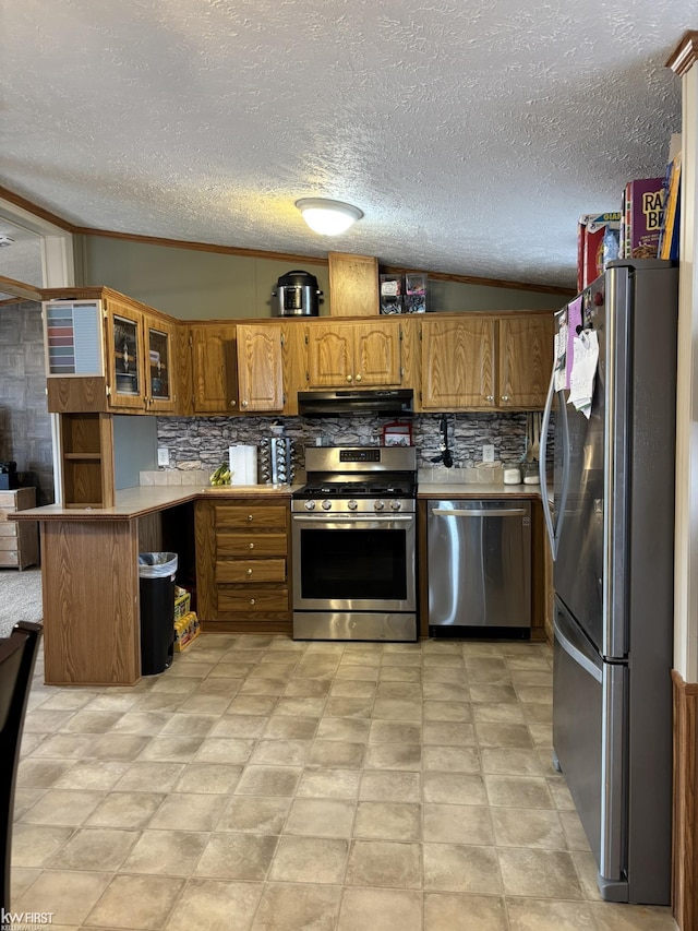 kitchen featuring appliances with stainless steel finishes, under cabinet range hood, brown cabinets, a peninsula, and decorative backsplash