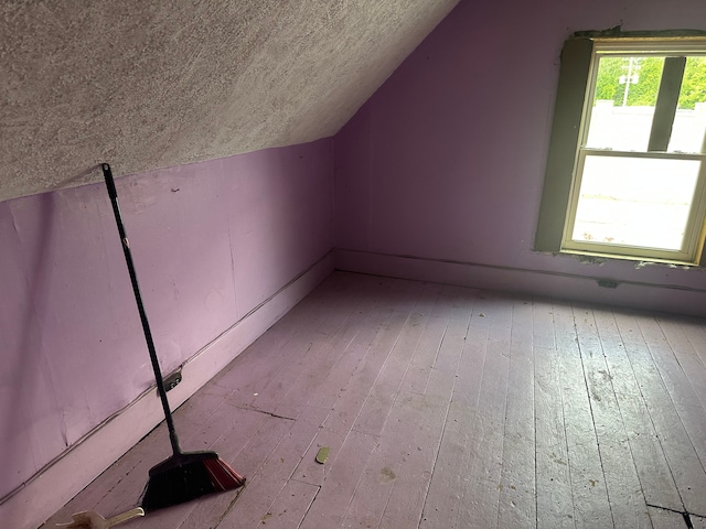 additional living space with vaulted ceiling, light wood-style flooring, and a textured ceiling