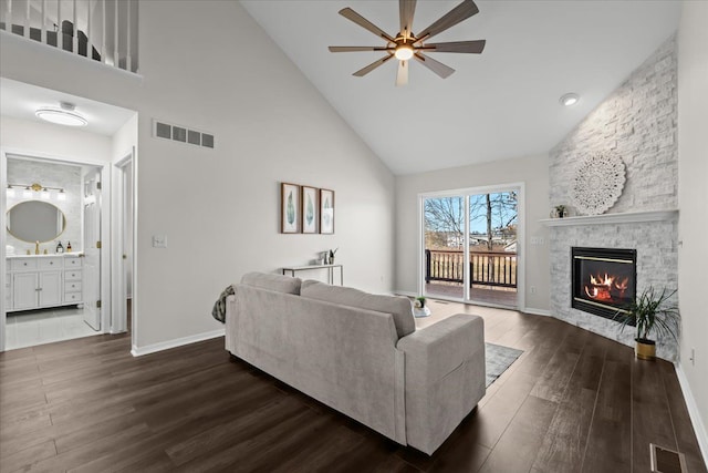 living room with visible vents, a stone fireplace, ceiling fan, and dark wood-style flooring