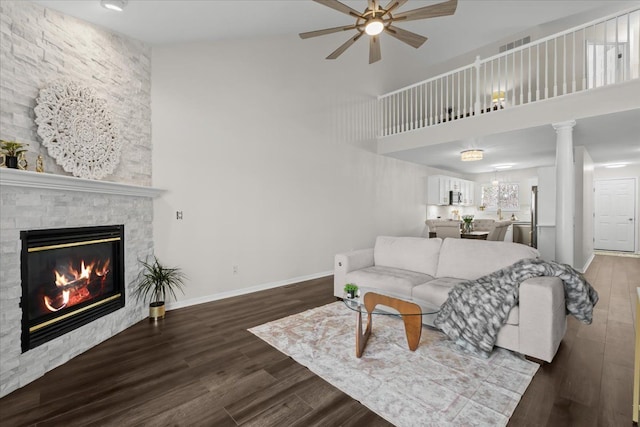 living room featuring a stone fireplace, wood finished floors, baseboards, and a ceiling fan