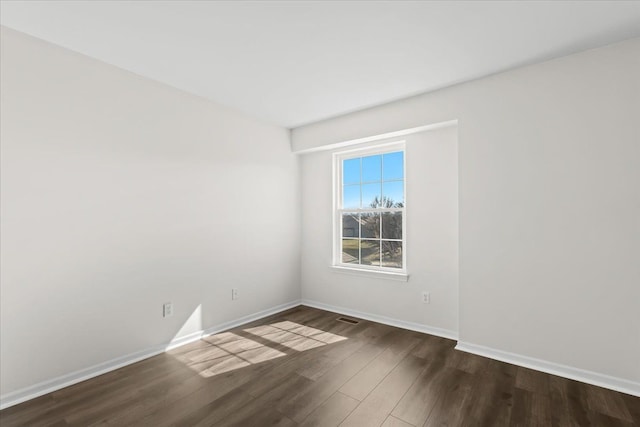 spare room featuring dark wood finished floors, visible vents, and baseboards