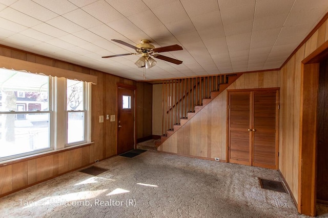 foyer featuring stairway, wooden walls, carpet flooring, and visible vents