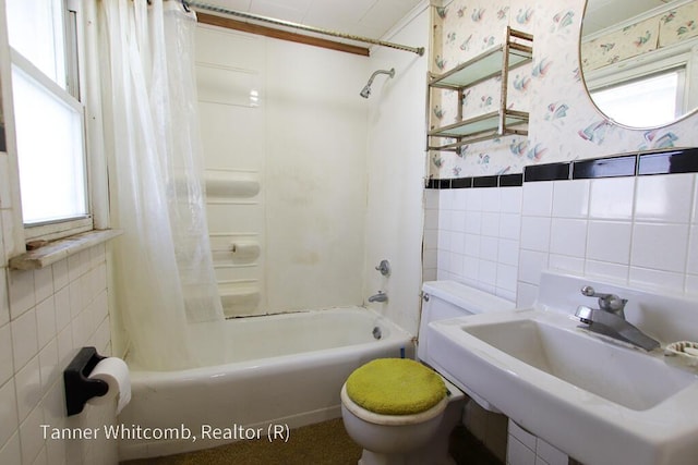 bathroom with wallpapered walls, a sink, tile walls, toilet, and shower / tub combo with curtain