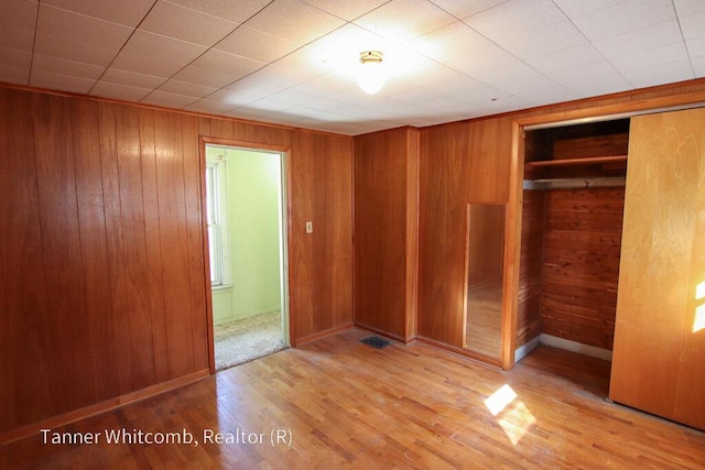 unfurnished bedroom featuring a closet, wood finished floors, baseboards, and wood walls