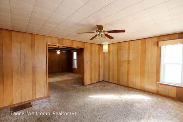 carpeted empty room featuring visible vents, wood walls, baseboards, and a ceiling fan