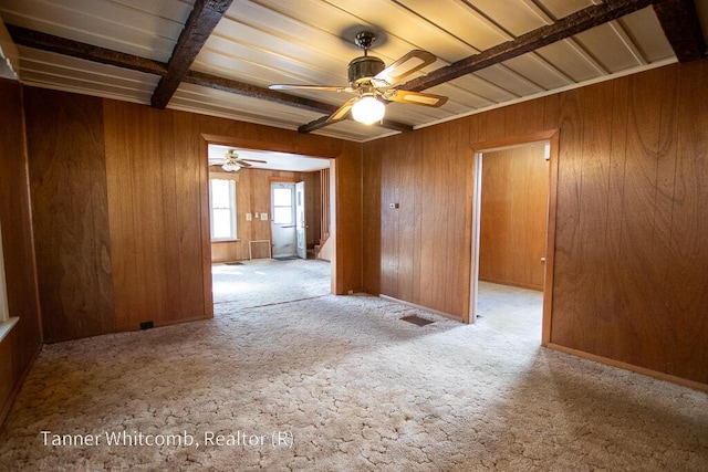 empty room with beam ceiling, visible vents, wood walls, and ceiling fan