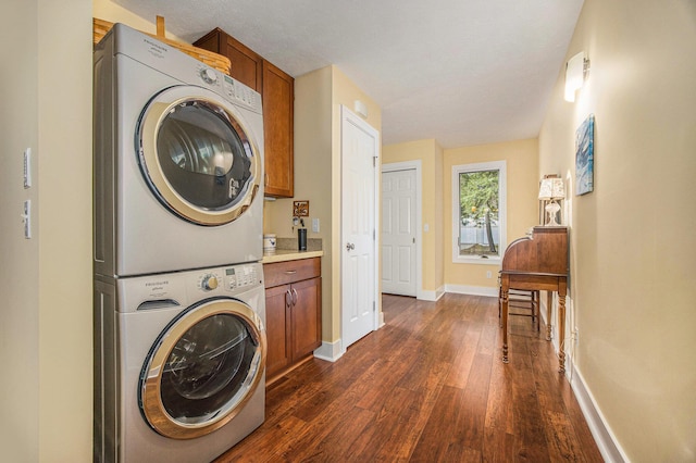 clothes washing area featuring cabinet space, baseboards, stacked washer and clothes dryer, and dark wood finished floors