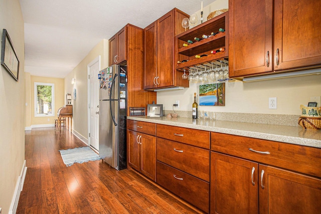 kitchen with open shelves, dark wood-type flooring, freestanding refrigerator, and brown cabinets