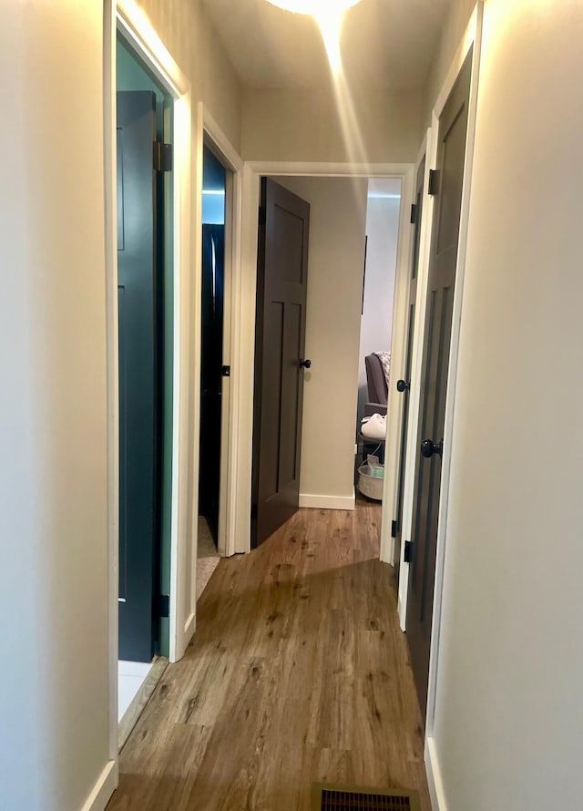 corridor with visible vents, wood finished floors, and baseboards