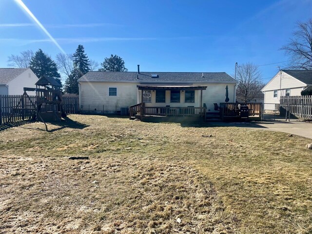 rear view of property featuring a wooden deck, a playground, a yard, and fence