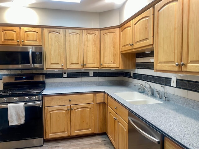 kitchen featuring backsplash, light countertops, light wood-style flooring, appliances with stainless steel finishes, and a sink