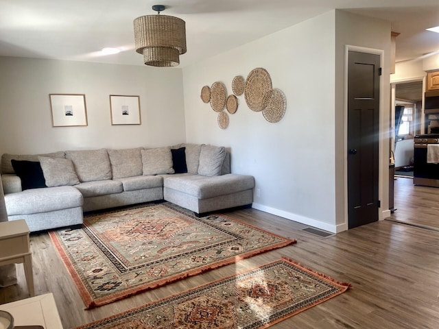 living area featuring a notable chandelier, wood finished floors, visible vents, and baseboards