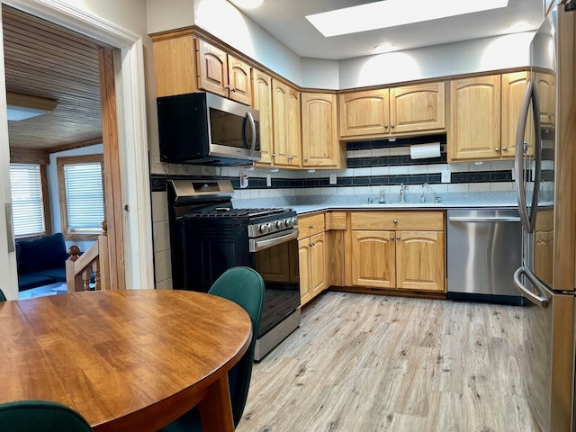 kitchen with light wood-type flooring, a sink, light countertops, appliances with stainless steel finishes, and tasteful backsplash