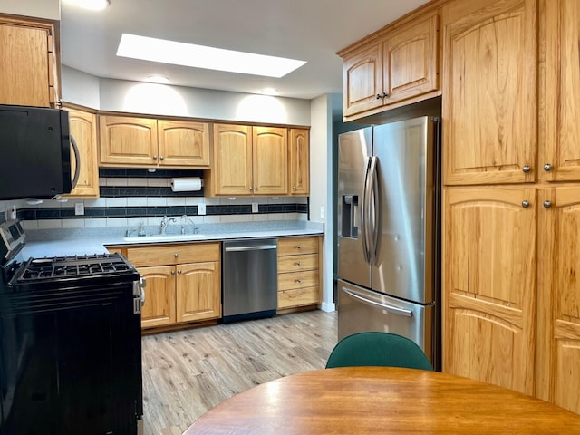 kitchen with light wood-type flooring, light countertops, decorative backsplash, black appliances, and a sink