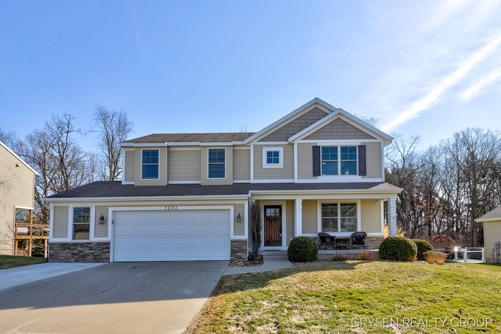 craftsman house featuring driveway, a front lawn, stone siding, covered porch, and an attached garage